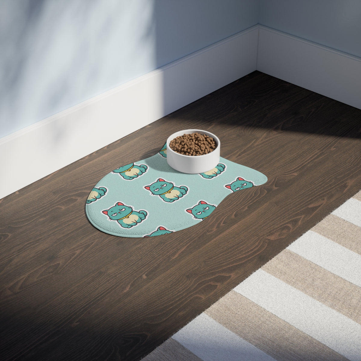 The Catch of the Day fish-shaped feeding mat on a wood floor with a bowl of kibble, showing the mint grumpy cat pattern.