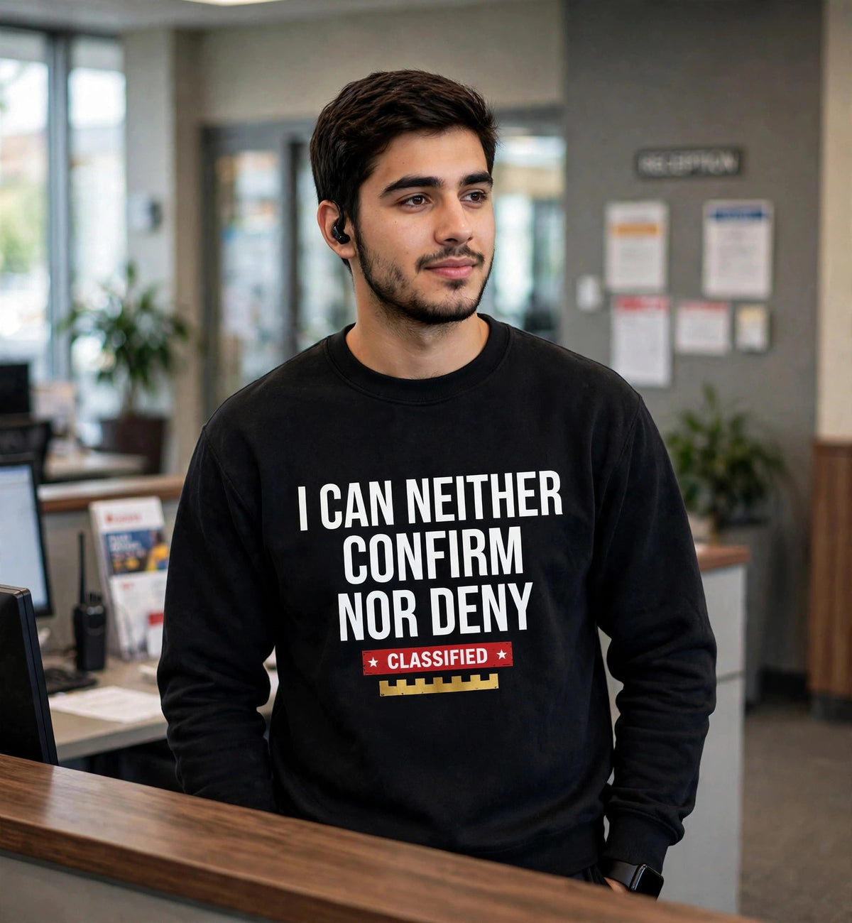 Man modeling the black Confirm Nor Deny sweatshirt at a reception desk, white text I CAN NEITHER CONFIRM NOR DENY fully visible
