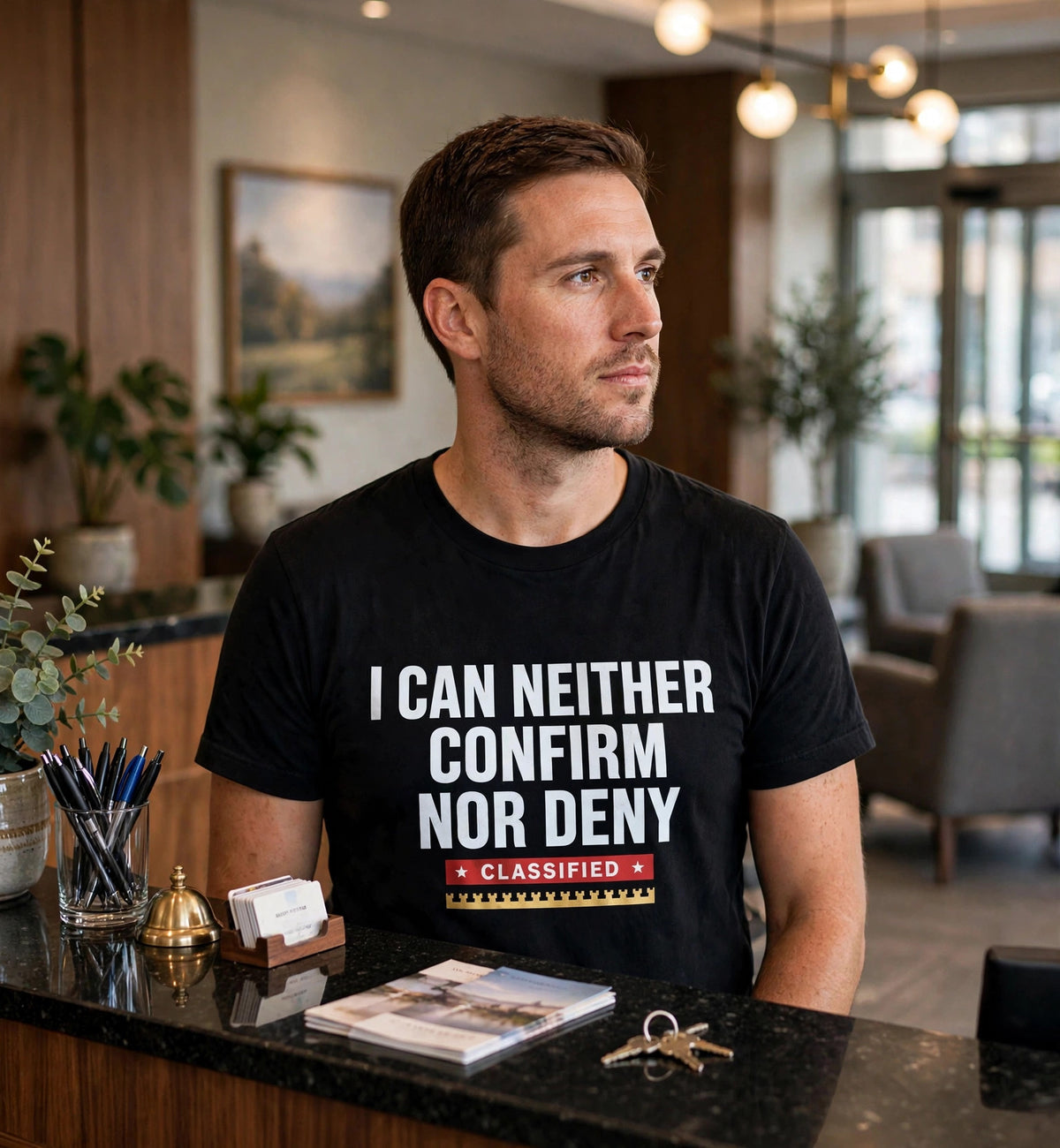 Man wearing the black I Can Neither Confirm Nor Deny t-shirt at a hotel reception desk