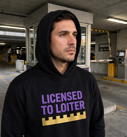 Man modeling the black Licensed To Loiter hoodie in a parking garage, purple print LICENSED TO LOITER with gold battlement strip fully visible