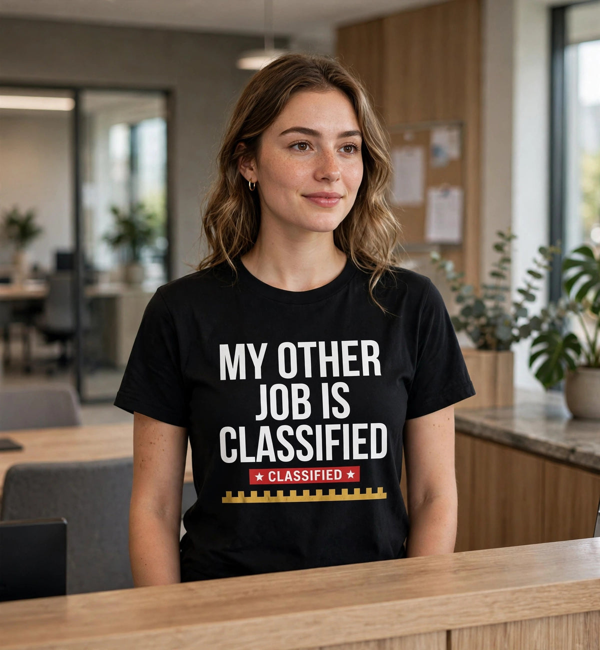 Woman wearing the black My Other Job Is Classified t-shirt at an office reception desk