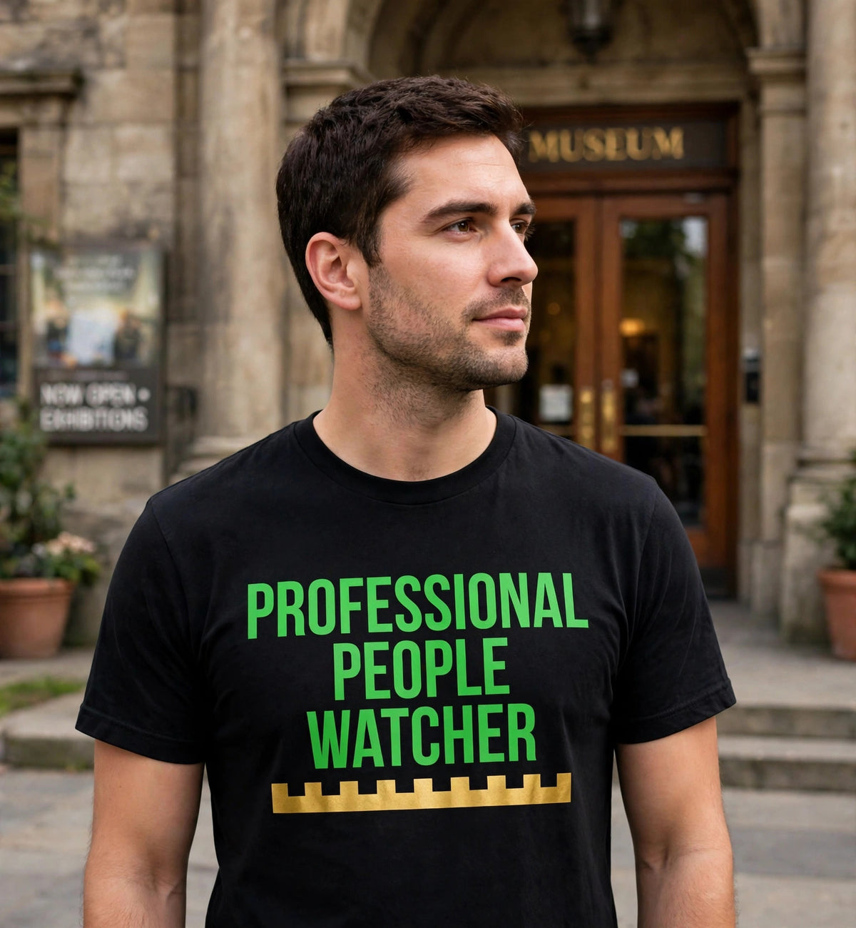 Man wearing the black Professional People Watcher t-shirt in green lettering outside a museum