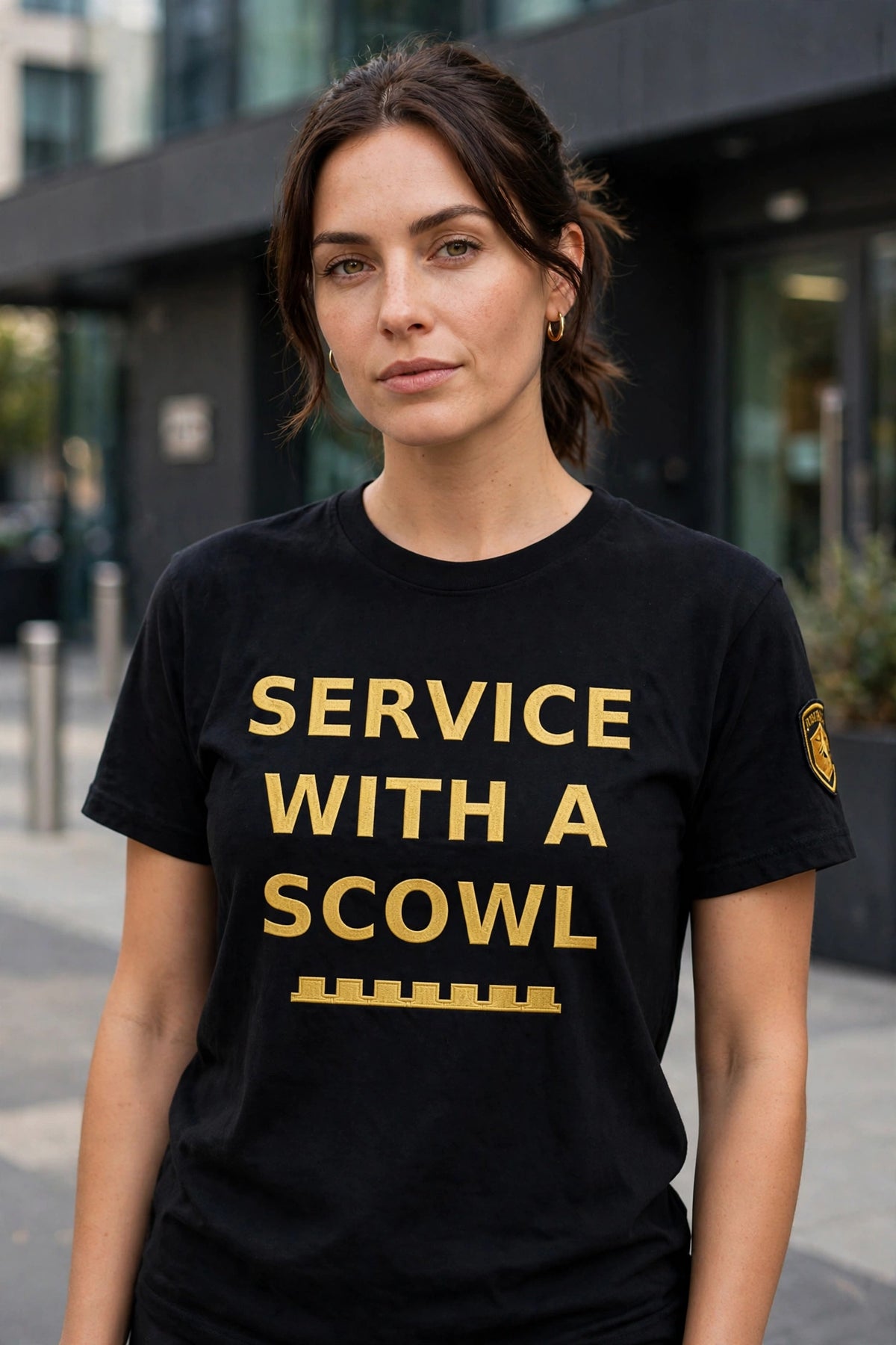 SERVICE WITH A SCOWL black t-shirt worn by a model — gold phrase text, battlements strip and sleeve insignia