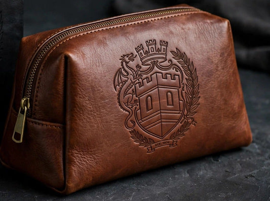 Sovereign Crest brown leather toiletry bag with engraved crest, staged on dark slate