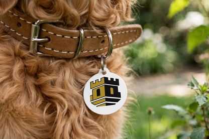 The Fortress ID tag hanging from a dog collar on a dog outdoors, showing the black and gold tower design.