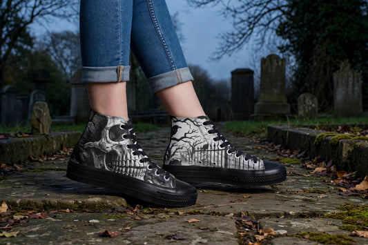 Person wearing Graveyard Shift skull cemetery high-top sneakers, side view, standing on a stone cemetery path at dusk