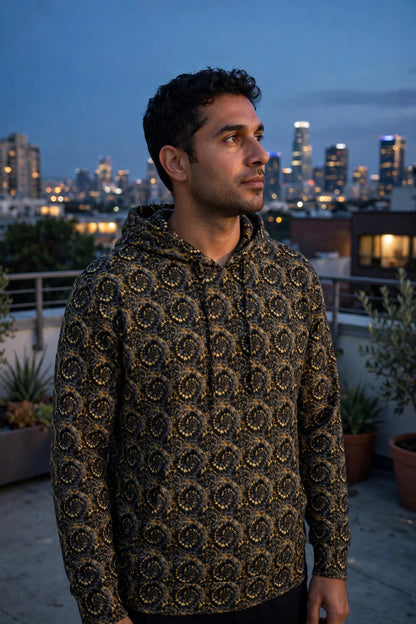 Man wearing the black and gold spiral pattern Rooftop hoodie on a terrace at dusk with a skyline behind him