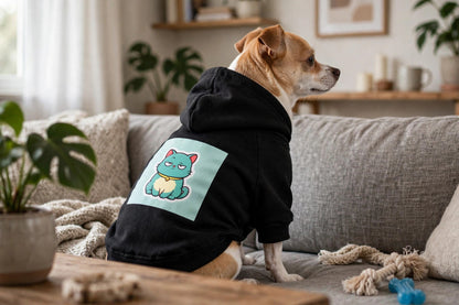 A small dog wearing the black Scowl pet hoodie on a sofa, showing the grumpy teal cat print on the back.