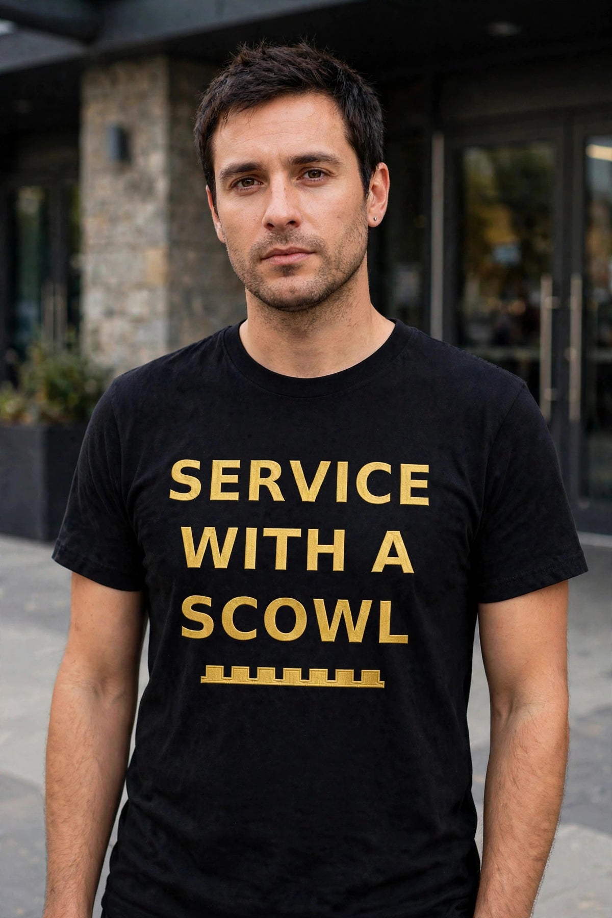 Man wearing the black Service With A Scowl t-shirt in gold lettering at a venue entrance