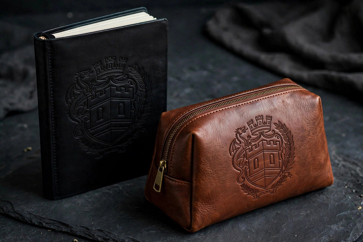 The Sovereign Crest Leather Set Two on dark slate seen from a closer angle: black leather journal and brown leather toiletry bag with the embossed crest